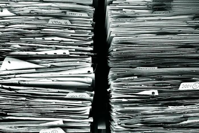 Stacks of dog-eared paper claim files, tagged by year, pressed together on a shelf