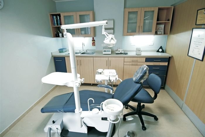 An empty dental treatment room: chair, overhead light, instrument tray and cabinetry